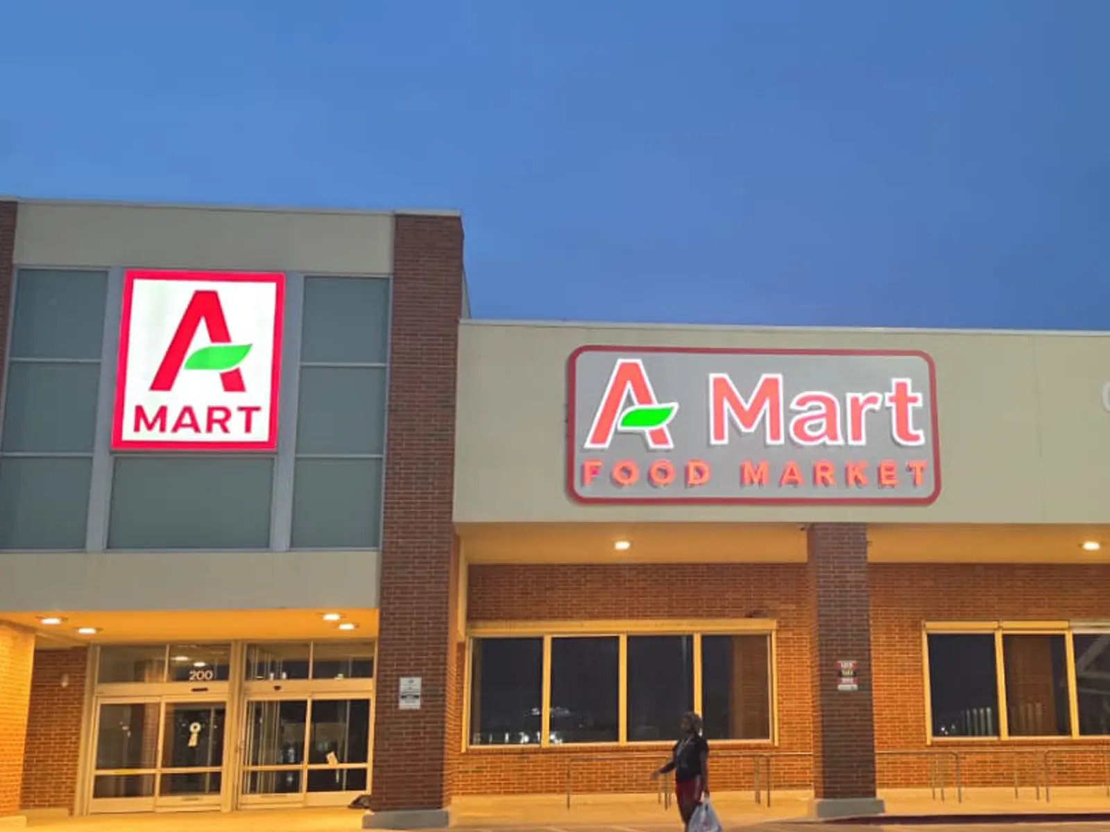 A Mart Food Market channel letters and a square logo box lit red and white at dusk above a grocery storefront
