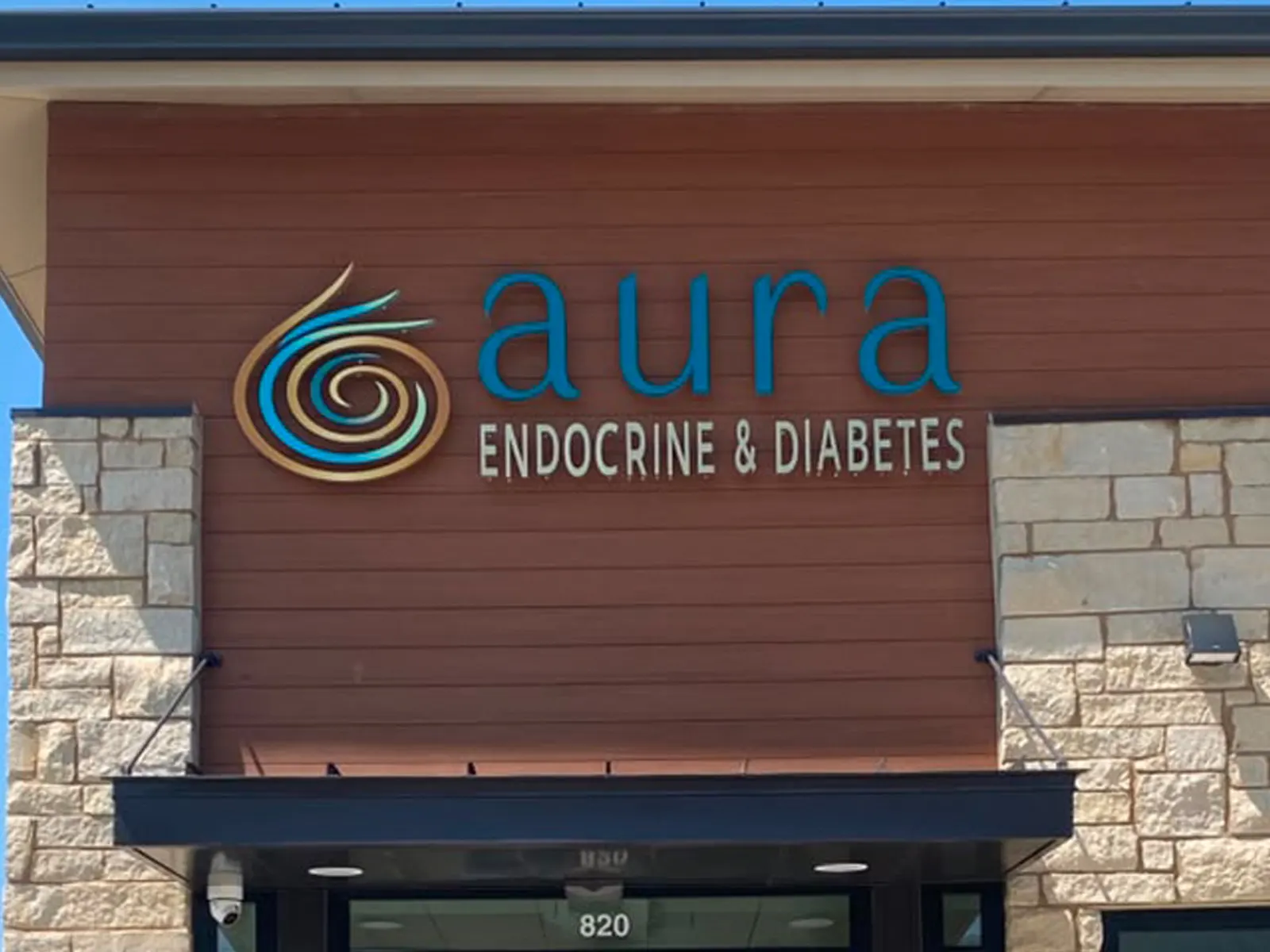 Aura Endocrine and Diabetes letters and spiral logo on a wood-look panel above a medical office entrance