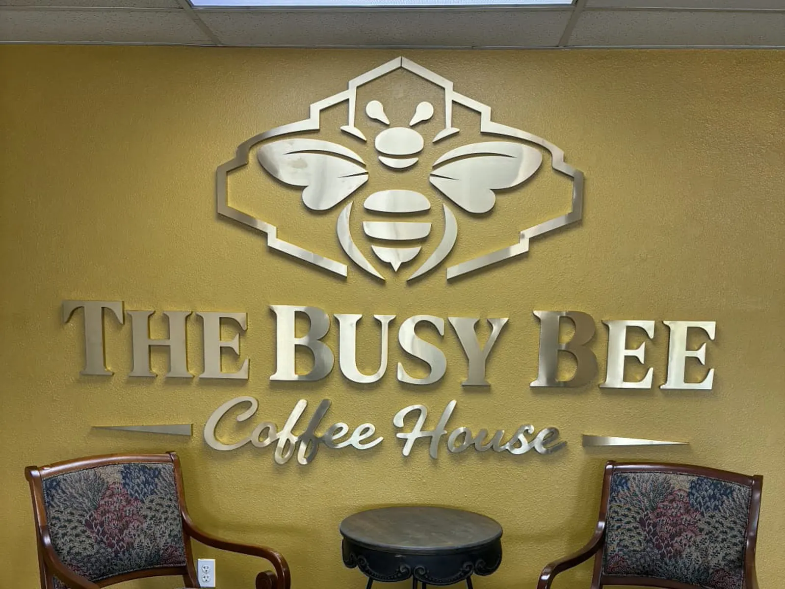 The Busy Bee Coffee House brushed metal bee logo and letters on a gold interior wall