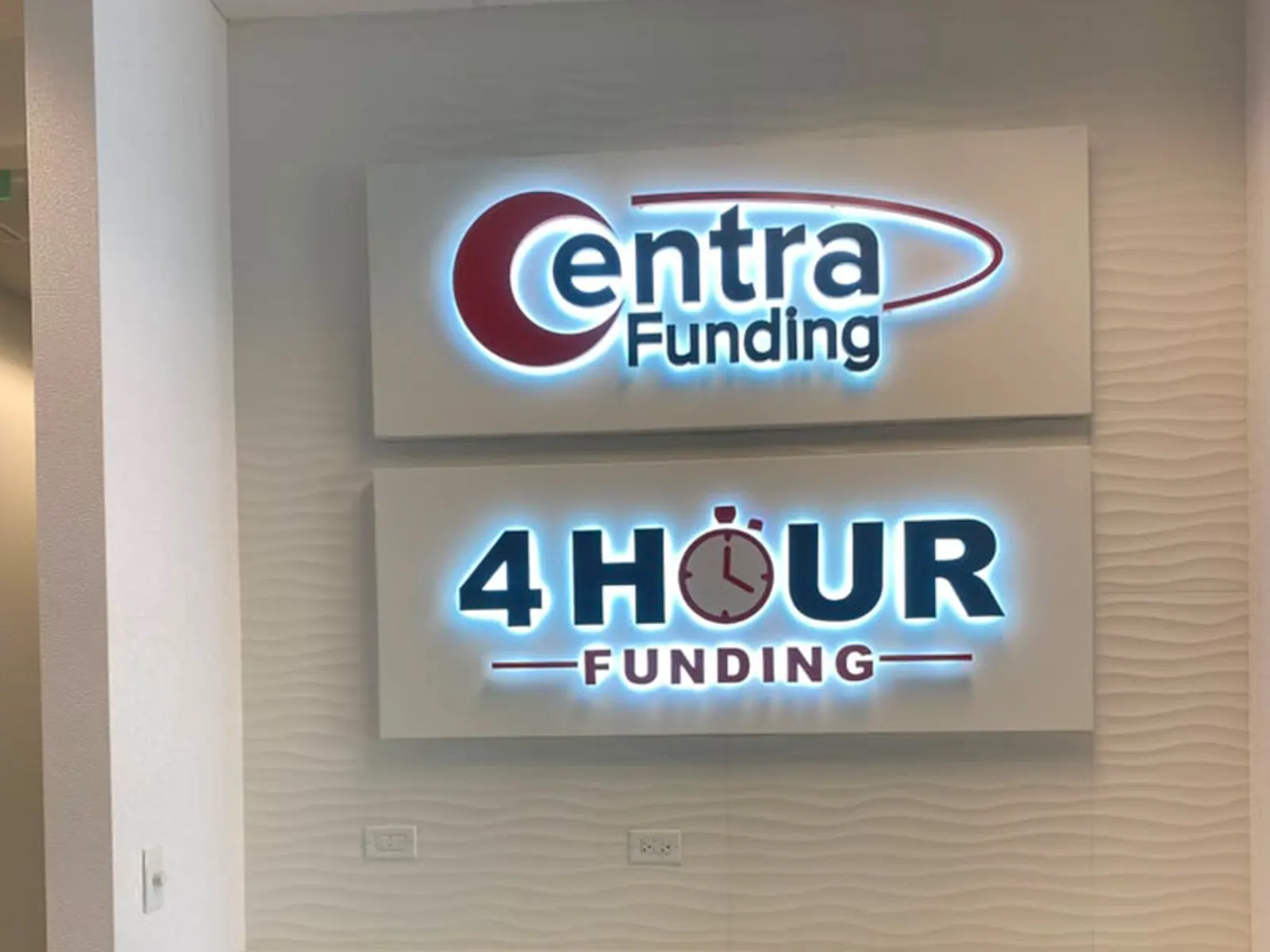 Centra Funding and 4 Hour Funding backlit logo panels mounted on a textured office wall