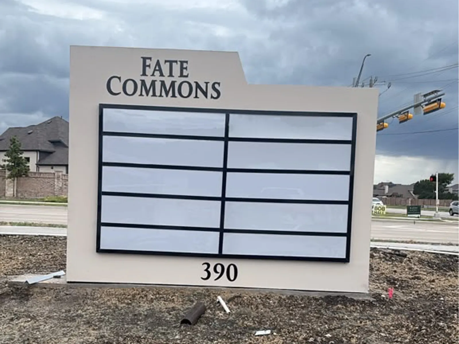 Fate Commons multi-tenant monument sign with a panel grid and address number 390 beside a road