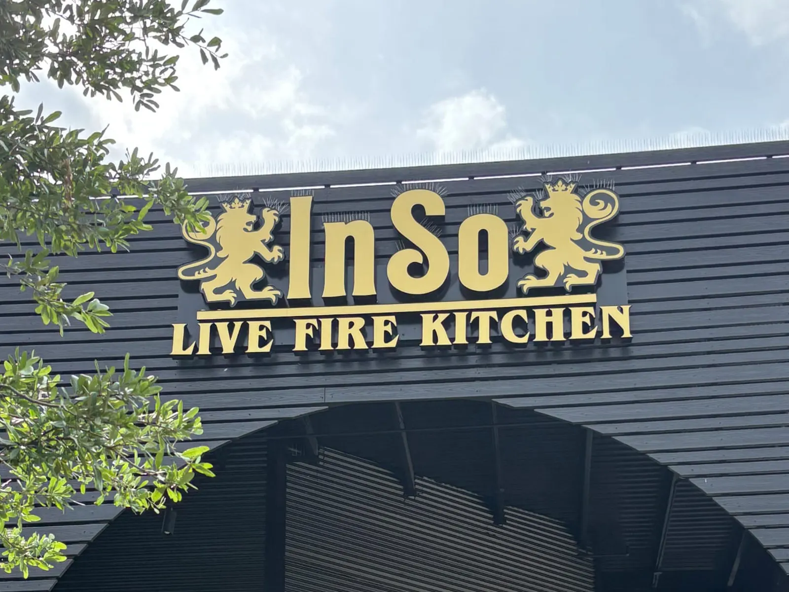InSo Live Fire Kitchen gold letters between two lion crests on a dark slatted facade