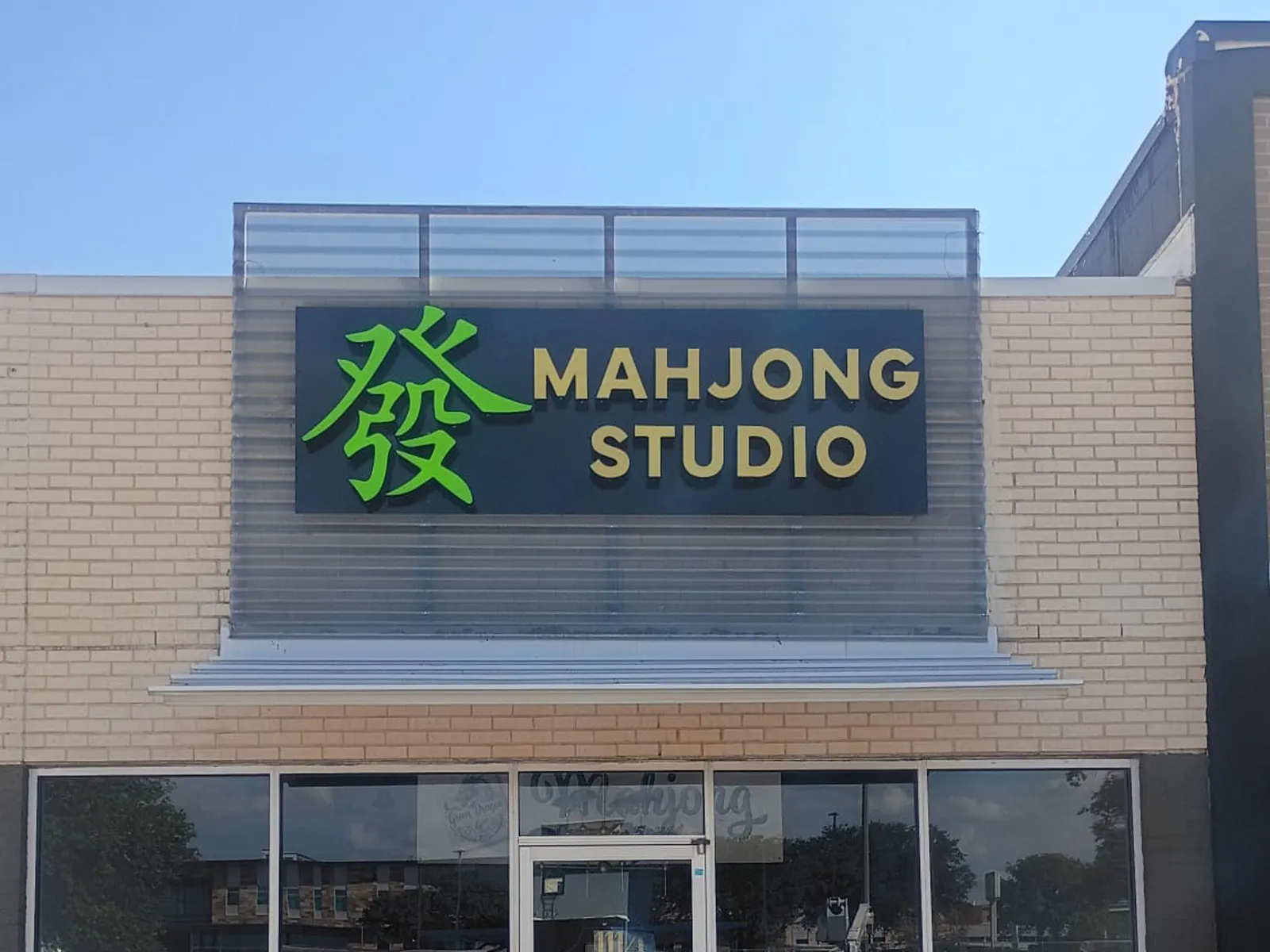 Mahjong Studio sign with a green character on a dark panel above a retail storefront