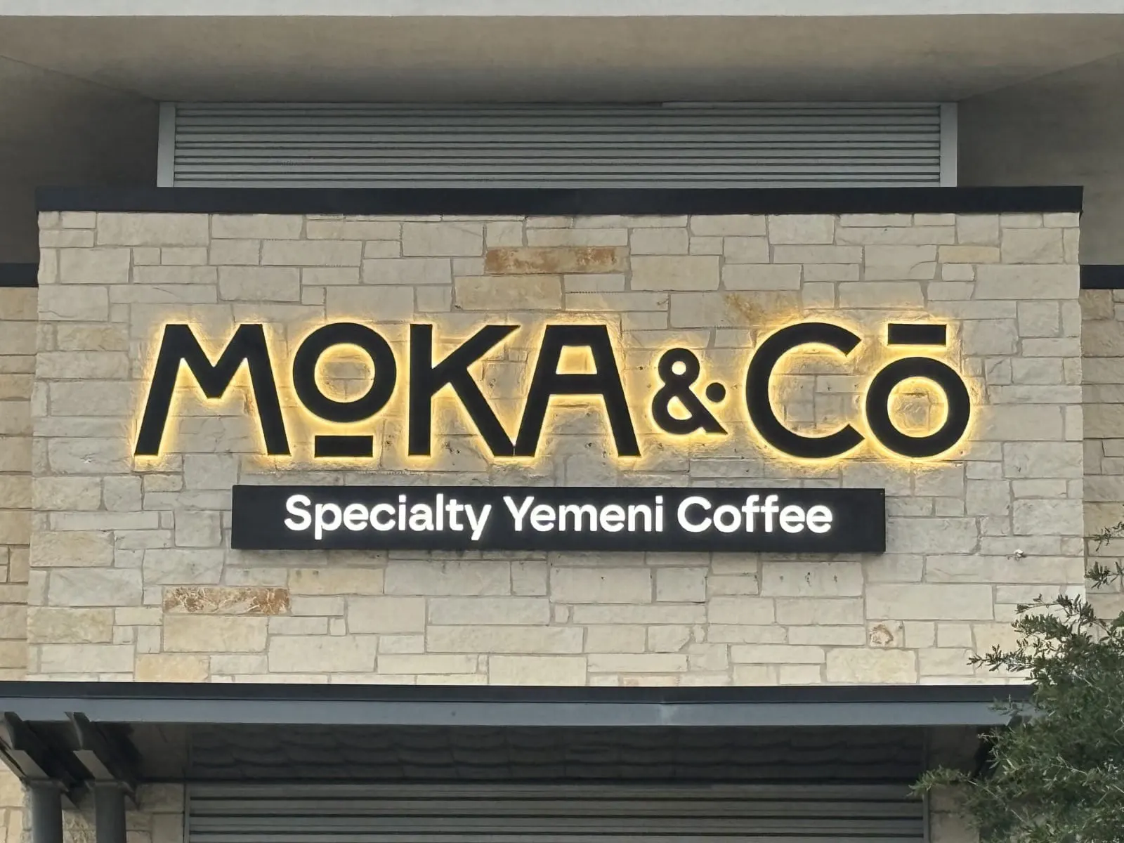 Moka and Co halo-lit letters with a lit Specialty Yemeni Coffee panel on a stone wall