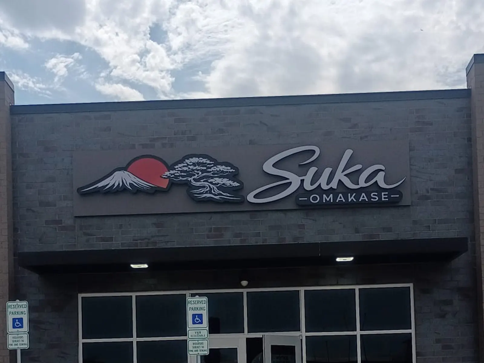 Suka Omakase sign with a mountain and bonsai logo on a dark brick restaurant facade