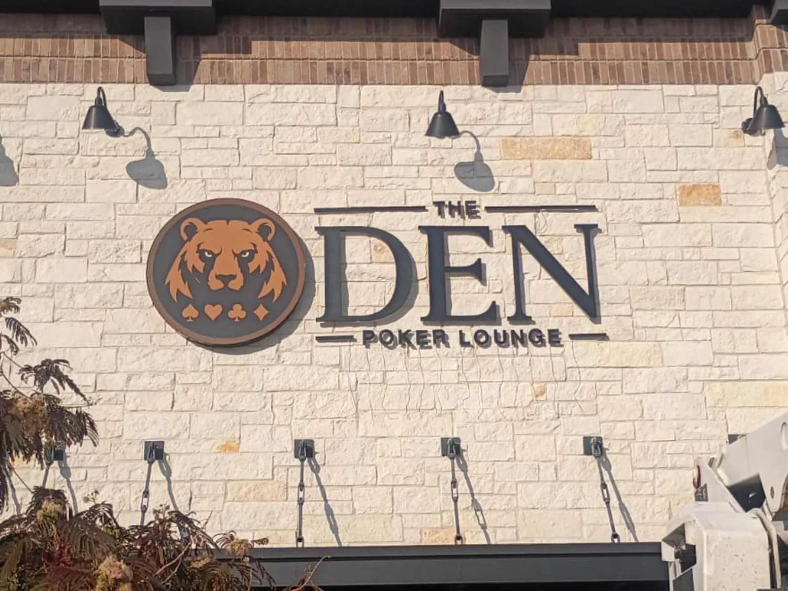 The Den Poker Lounge bear logo and dark dimensional letters on a limestone wall